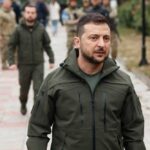 Zelensky walking outdoors with military personnel nearby.