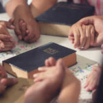 People holding hands with Bibles on table