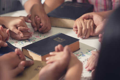 People holding hands with Bibles on table