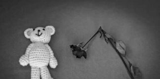 Crocheted bear and wilted rose on gray background