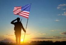 soldier holding flag facing sunset