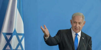Man speaking next to Israeli flag.