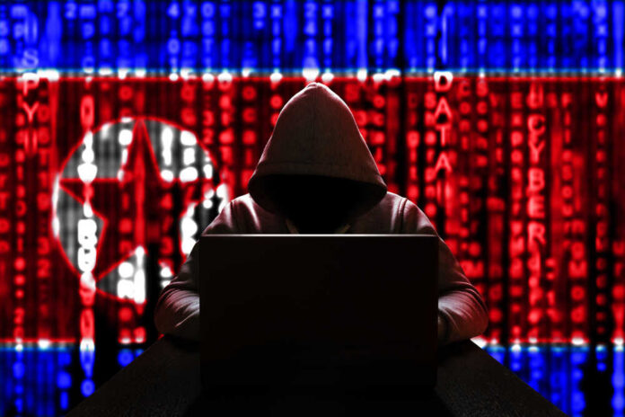 A hooded figure working on a laptop with a digital background featuring North Korean symbols