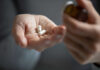A hand holding white capsules with a pill bottle in the other hand