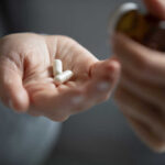 A hand holding white capsules with a pill bottle in the other hand