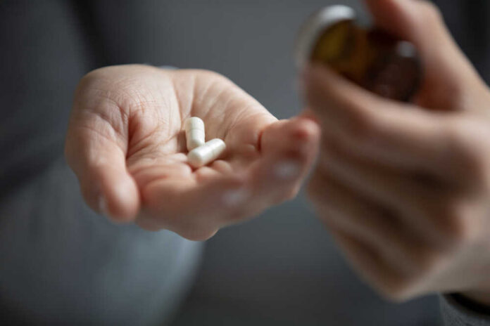 A hand holding white capsules with a pill bottle in the other hand