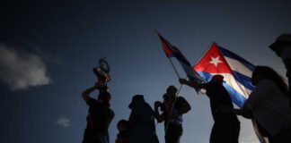 Silhouetted figures holding a trophy and Cuban flags during a celebration