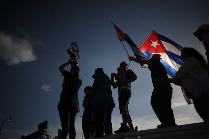 Silhouetted figures holding a trophy and Cuban flags during a celebration