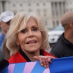 A woman with blonde hair and a red jacket participating in a protest