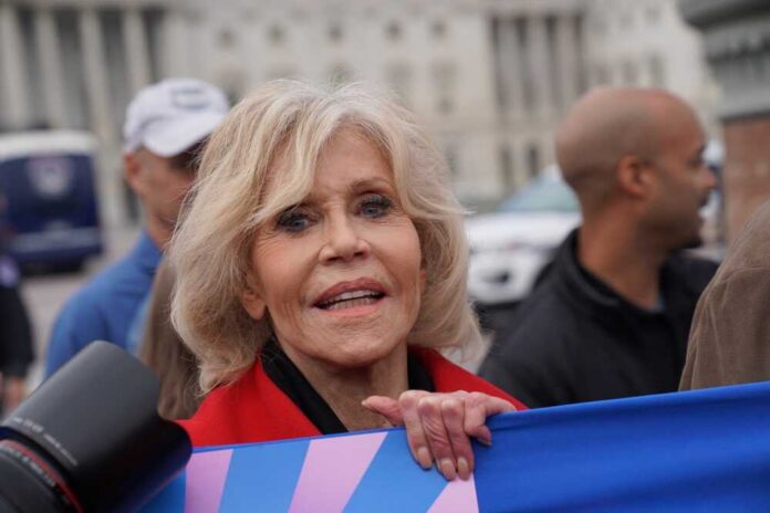 A woman with blonde hair and a red jacket participating in a protest