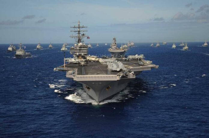 An aircraft carrier surrounded by various naval vessels in the ocean