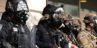 Police officers in tactical gear and gas masks standing in formation