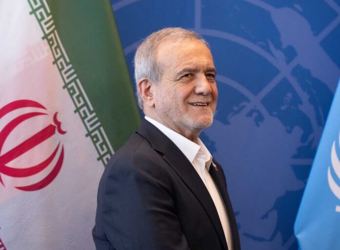 A man smiling in front of flags at a diplomatic event