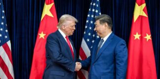 Two political leaders shaking hands in front of national flags