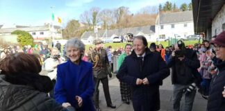 A group of people at a public event, with two individuals shaking hands and smiling.