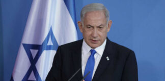 Man speaking in front of Israeli flag backdrop