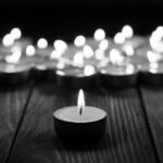 Teen Counselors Unprepared in Fatal Camp Flood Single candle burning among many on wooden surface.