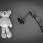 Crocheted bear and wilted rose on gray background