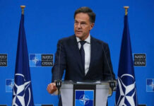Iran Conflict: NATO’s Deepest Rift in Decades Man speaking at podium with NATO flags behind him