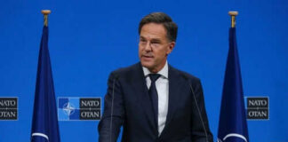 Man speaking at podium with NATO flags behind him