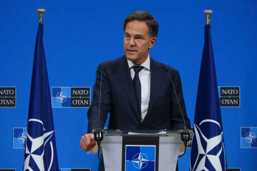 Man speaking at podium with NATO flags behind him