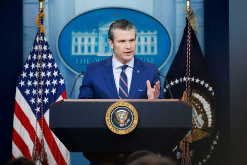 Man speaking at podium with flags in background