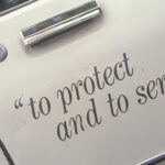 Close-up of a police vehicle door with the phrase 'to protect and to serve'