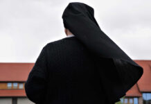 A nun in black attire standing outdoors with a cloudy sky in the background