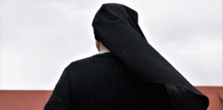 A nun in black attire standing outdoors with a cloudy sky in the background