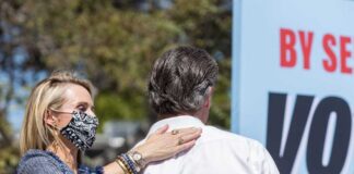 A woman in a mask places her hand on a man's shoulder at a political event