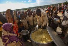 Children and adults gathered around a large pot of food during a distribution event