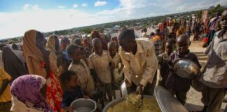 Children and adults gathered around a large pot of food during a distribution event