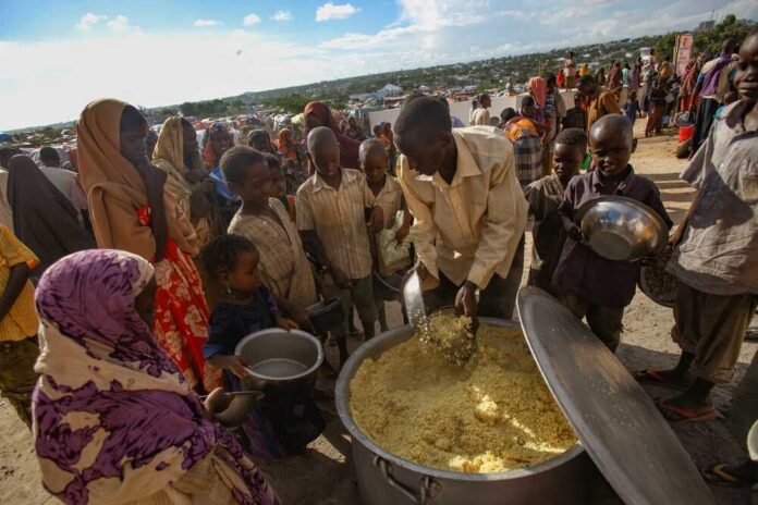 Children and adults gathered around a large pot of food during a distribution event