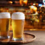Two glasses of beer on a wooden tray in a bar setting
