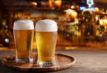 Two glasses of beer on a wooden tray in a bar setting
