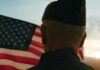 A veteran in uniform standing in front of an American flag at sunset
