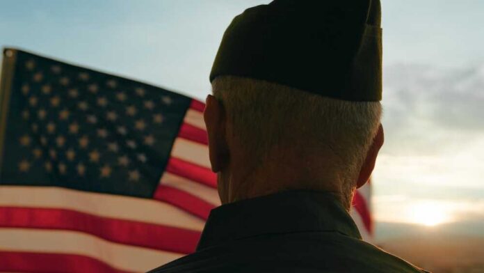 A veteran in uniform standing in front of an American flag at sunset