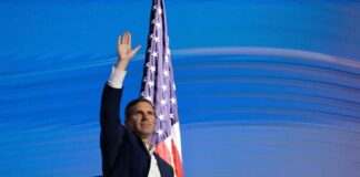 A man waving his hand in front of an American flag at a public event