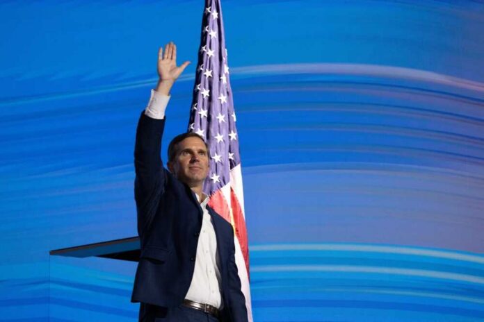 A man waving his hand in front of an American flag at a public event