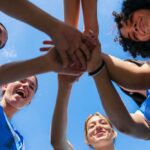 Trump RESCUES College Sports From Total Collapse Group of female athletes joining hands in a circle under a blue sky