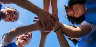 Group of female athletes joining hands in a circle under a blue sky