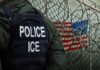 U.S. Citizen Dragged Out – ICE Faces Backlash Police officer in tactical gear standing near a barbed wire fence with an American flag in the background