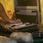 A person packing items into a suitcase in a dimly lit room