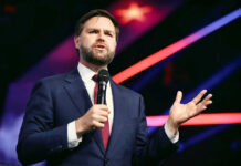 Man in suit speaking with microphone on stage.