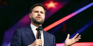 Man in suit speaking with microphone on stage.