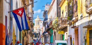 Colorful street scene with Cuban flag and people.