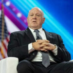 Homan Weighs Force-Feeding Detainees — ‘Hunger Strikes Won’t Change Anything’ Man in suit sitting on stage with American flag.