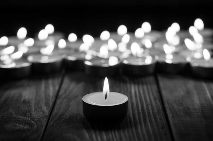 Single candle burning among many on wooden surface.