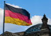 Palantir’s NATO Grip Threatened by German Rebellion German flag waving against a blue sky near a historic building