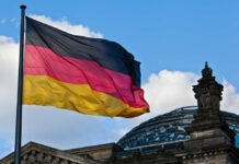 Palantir’s NATO Grip Threatened by German Rebellion German flag waving against a blue sky near a historic building